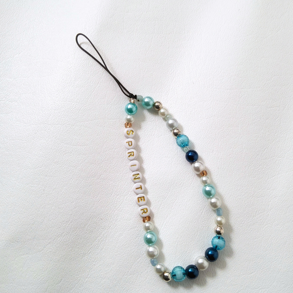 "A beaded phone charm with a mix of white pearls, aqua blue, and navy-blue beads. White letter beads spell out 'SPRINTER' with a black cord to attach the charm to your phone case."